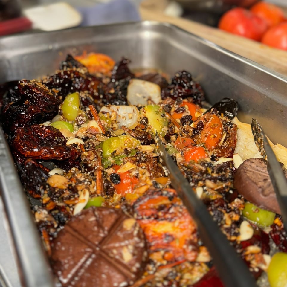 Roasted vegetables and assorted ingredients coated with seeds and spices in a stainless-steel restaurant prep tray.