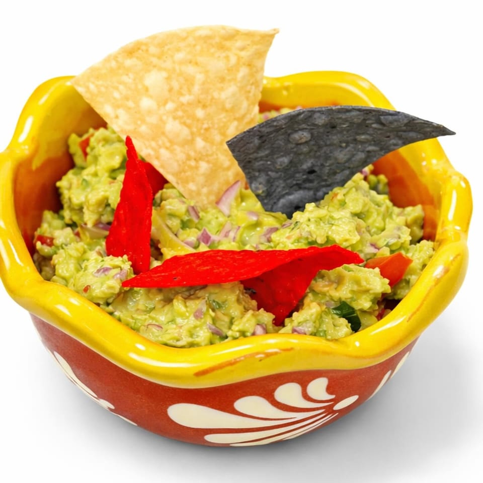 Guacamole topped with red pepper strips and tortilla chips in a colorful ceramic bowl.