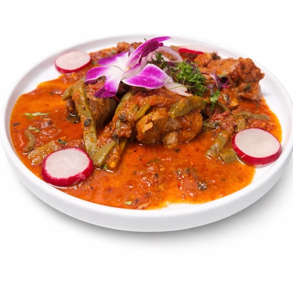 Plate of tender meat and green peppers in a rich red sauce, garnished with radishes, microgreens, and purple orchid petals.